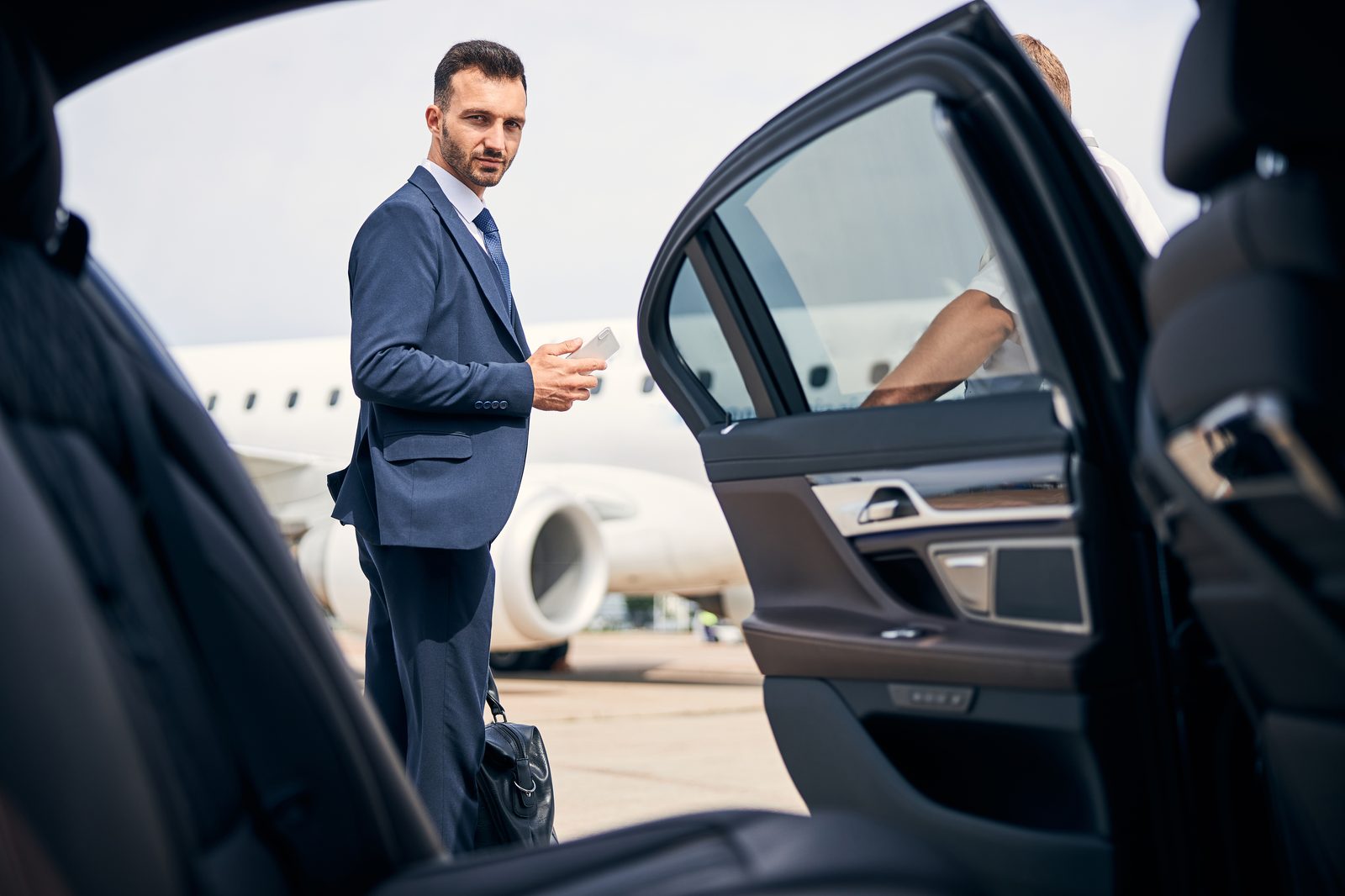 Executive boarding a Business Class sedan at a private aviation terminal